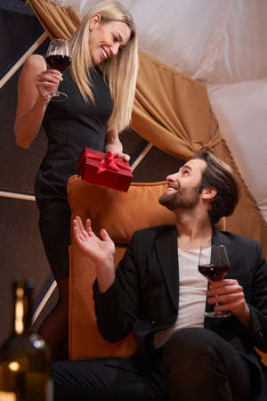 Female passing gift box to her partner in armchair