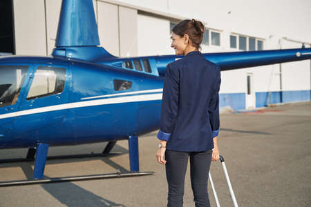 Smiling young woman with luggage looking at helicopterの写真素材