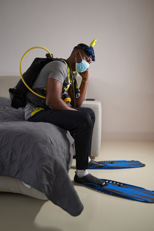 Scuba diver in medical mask sitting on bedの写真素材