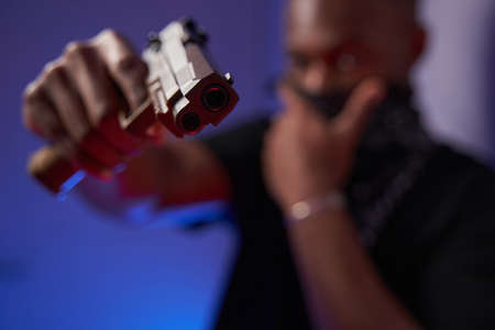 Person pointing a gun at camera in studio