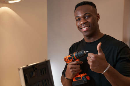 Multiracial man with drill showing thumbs-up to cameraの写真素材