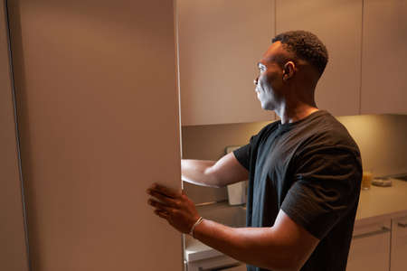 Multiracial man reaching inside kitchen cabinet with handの写真素材