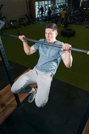 Concentrated male athlete performing pull-ups at gym