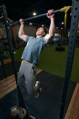 Focused calm young male gymnast doing pull-ups