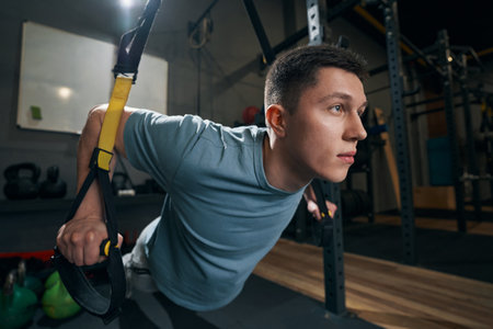 Concentrated strong man exercising on suspension trainer