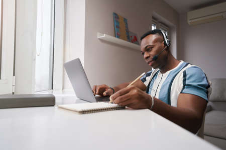 Man at home working at laptop and making notes