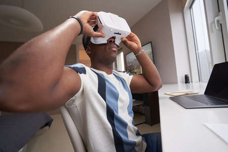 Multiracial man in VR glasses looking around his home workplace