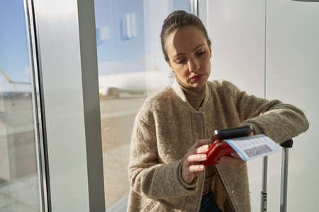 Woman waiting inside airport with boarding pass and smartphoneの写真素材
