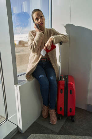 Worried woman speaking on the phone while holding documentsの写真素材