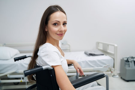 Pleased female patient seated in wheeled chair posing for cameraの写真素材
