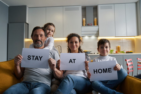 Pleased family showing paper signs to camera from sofaの写真素材