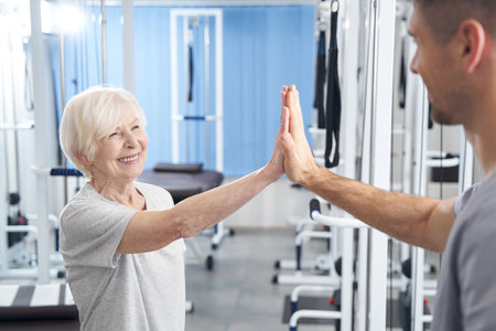 Satisfied pensioner high fiving male medic and smiling