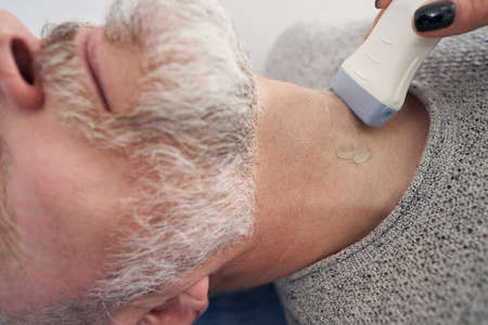 Professional Caucasian diagnostician performing thyroid ultrasound examinationの写真素材