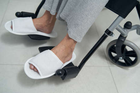 Disabled person in slippers sitting in manually-propelled chair