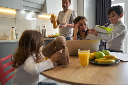 Woman working on laptop looking with terror on son homeworkの写真素材