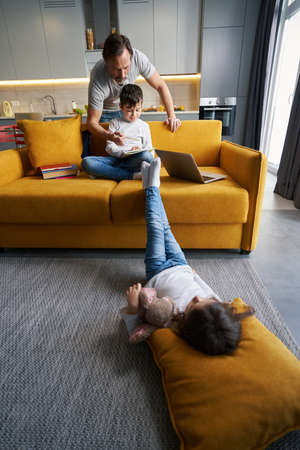 Boy and father doing homework while girl lying on floorの写真素材