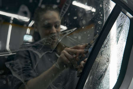 Detailer trimming off clear windshield protective film on car windowの写真素材