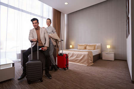 Happy tourist couple with luggage in hotel roomの写真素材