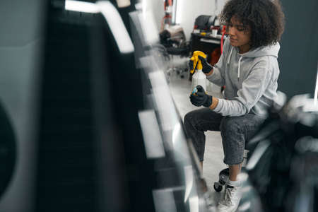 Female worker wetting car exterior with lubricating agent