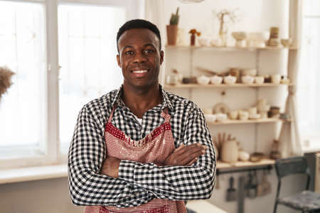Cheerful young potter standing in his pottery workshopの写真素材