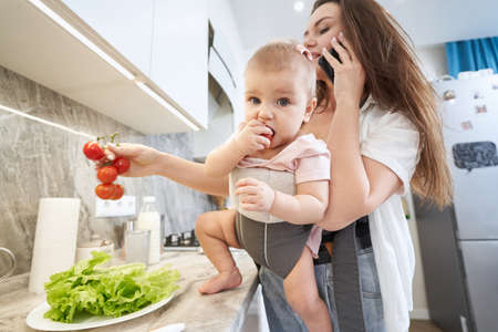 Multitasking Caucasian mother talking on the phone while spending time with kid at homeの写真素材
