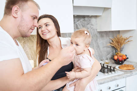 Beautiful brunette mother with baby girl in hands while looking to her husband in the room indoorsの写真素材