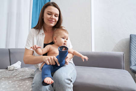 Caring mother putting jeans on baby legs