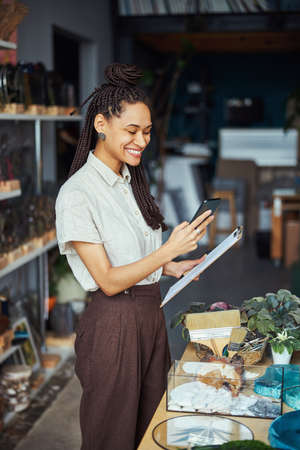 Pleased floral decorator reading a text message on her cellphoneの写真素材