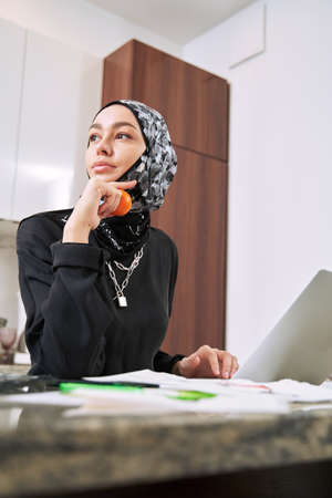 Relaxed muslim woman with tangerine and notebook indoorsの写真素材