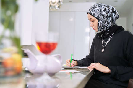 Young muslim woman with laptop using pen at home