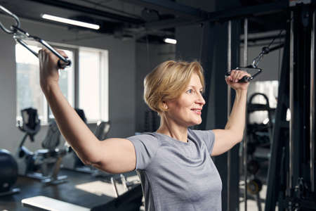 Cheerful woman using gym trainer in fitness centerの写真素材