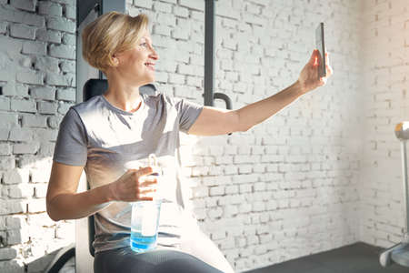 Cheerful woman taking picture with smartphone in gymの写真素材