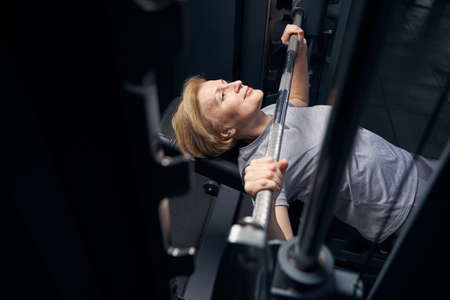 Woman using barbell press bench machine in gym