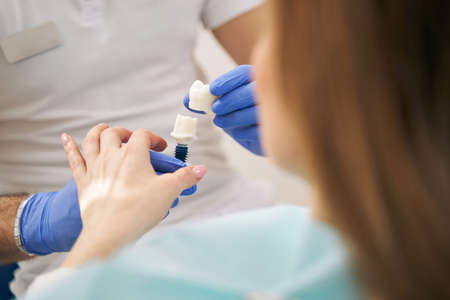 Dentist showing dental implant to woman in clinicの写真素材
