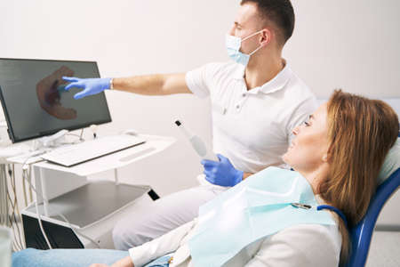 Male dentist showing results of dental 3D scanning to woman in clinicの写真素材
