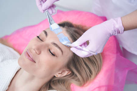 Cosmetologist applying mask on female client skin