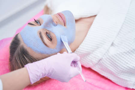 Gloved hand applying mask to woman skin
