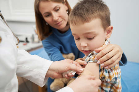 Doctor placing medical plaster on child arm after vaccinationの写真素材