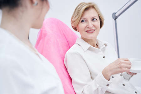 Happy aged woman enjoying communication with cosmetologistの写真素材
