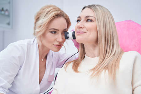 Dermatologist using dermoscopy equipment on client skin