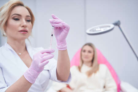 Beauty clinic doctor preparing for giving injection to female patientの写真素材