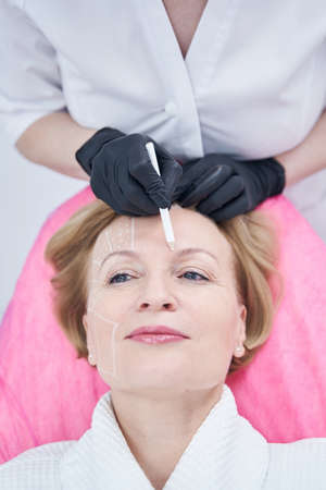 Beautician drawing marks on woman face in cosmetology clinic