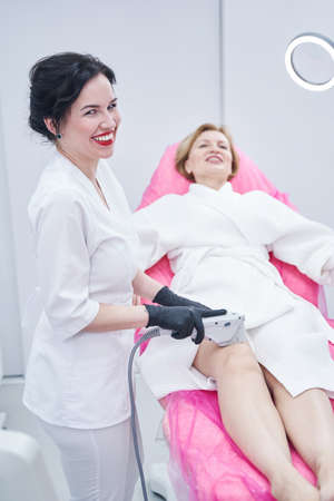 Cheerful beautician performing ultrasound lifting procedure clinicの写真素材