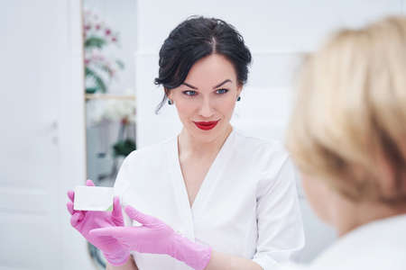 Female cosmetologist showing cosmetic cream to client in spa salonの写真素材