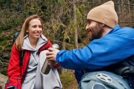 Man sharing tea in a flask with woman in forest