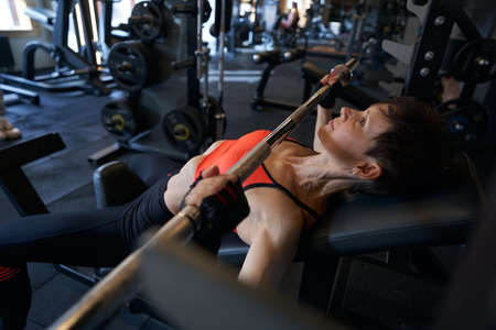 Professional female athlete bench-pressing in fitness studio