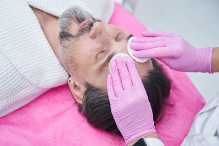 Female cosmetologist wiping adult patient face before cosmetic procedureの写真素材