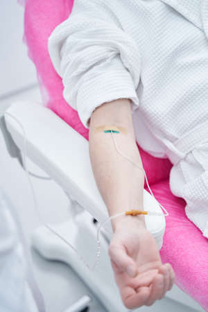 Male client in white bathrobe receiving professional IV infusion in clinic