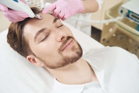 Male enjoying ultrasonic cleansing procedure on forehead