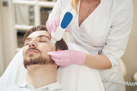 Beautician removing oil and dirt from pores with ultrasound technologyの写真素材